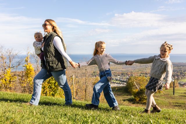 A mom and her three daughters hold hands as they walk across the mountaintop on a sunny fall afternoon.