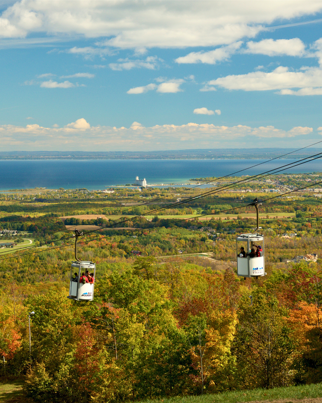 A beautiful view of the open-air gondolas ascending up the Mountain across the amber and auburn forest on a sunny fall afternoon at Blue.