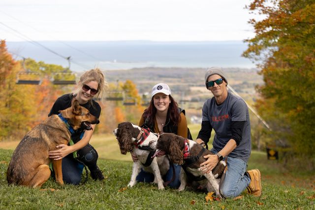 A group of three friends and their dogs smiling for a photo at the lookout on Village Way Hiking Trail on a fall afternoon.