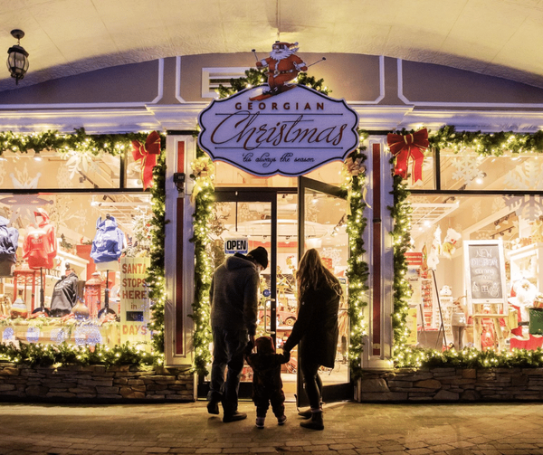 Parents holding hands with their toddler, standing outside the Georgian Christmas storefront decorated for the holidays.