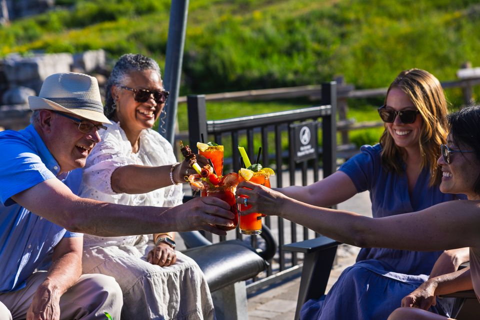 Group of friends cheers their cocktails together on the 1858 Caesar Bar patio at the base of the mountain.