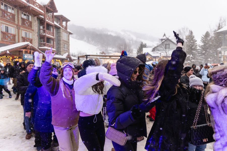 Group of people laughing and dancing in a conga line on a snowy afternoon.