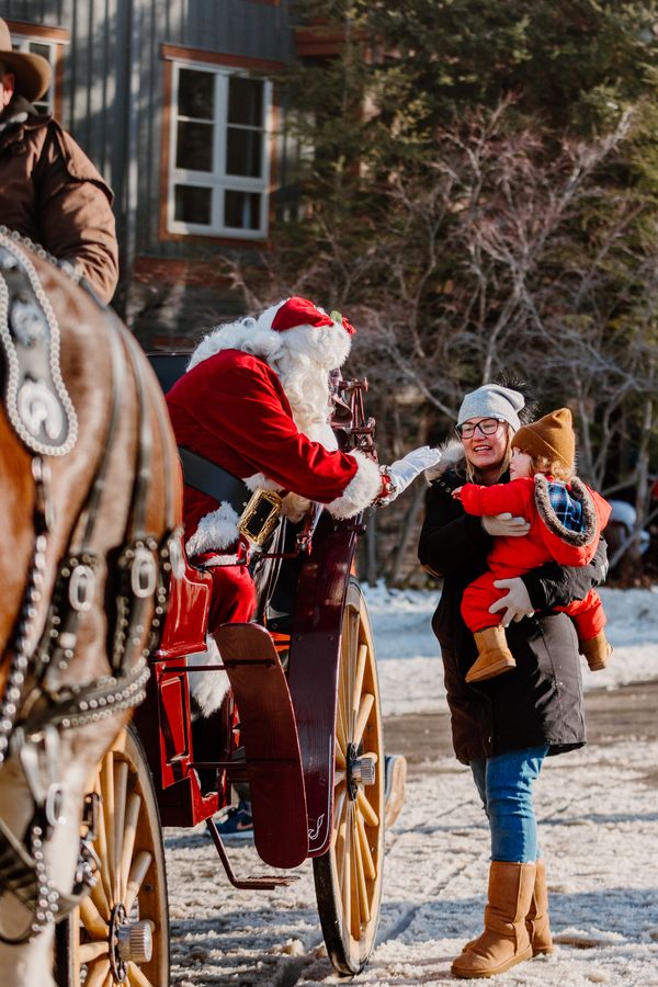 Mom holding her toddler up to see Santa on his horse & carriage during Holiday Magic in the Village.