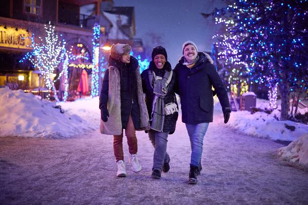 Group of adult friends laughing while strolling through the snow covered streets, taking in the Holiday Magic Light Trail