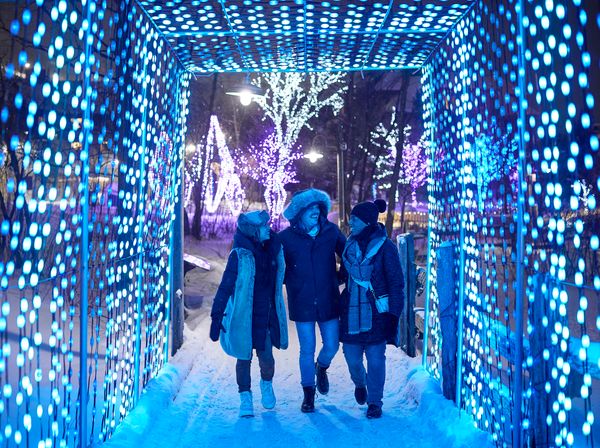 Group of 3 friends smiling in awe as they walk through a tunnel of blue lights along the Holiday Magic Light Trail.