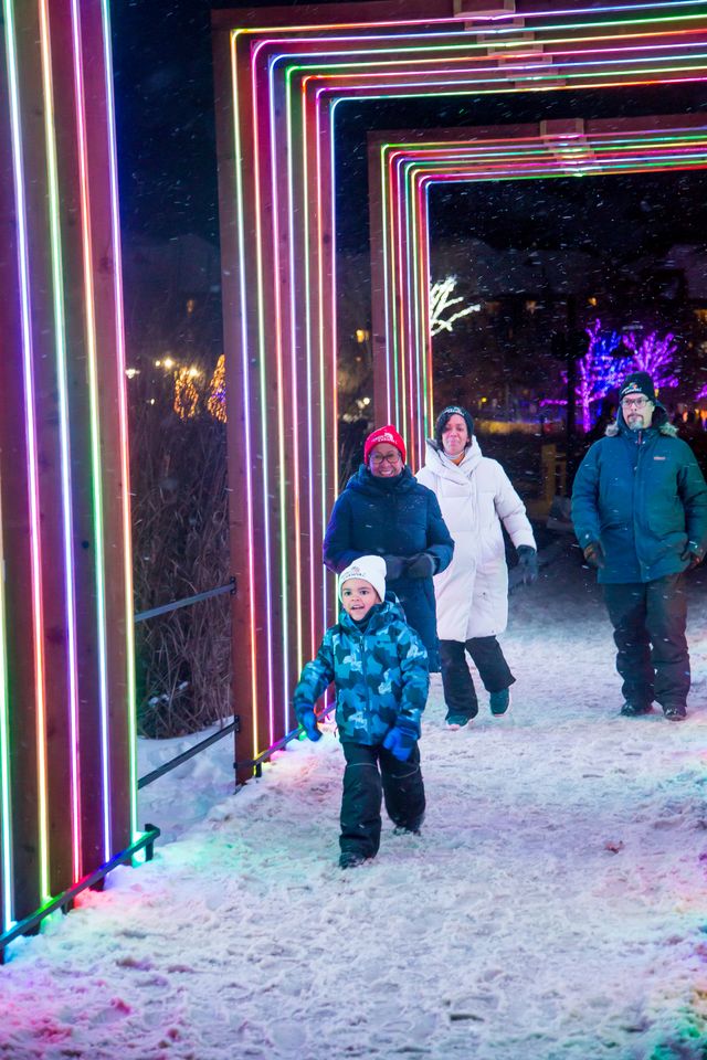 Family walking beneath multi-coloured installation along the Blumination Light Trail at Blue Mountain Village.