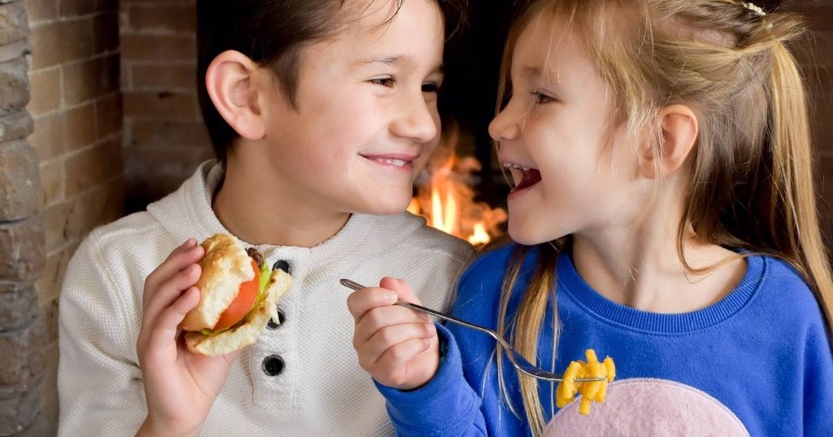 Two kids enjoying dinner at Kaytoo, sitting by the fireplace.