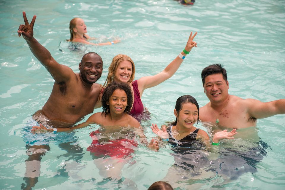 Two families smiling and splashing together in the outdoor pool at Plunge Aquatic Centre.
