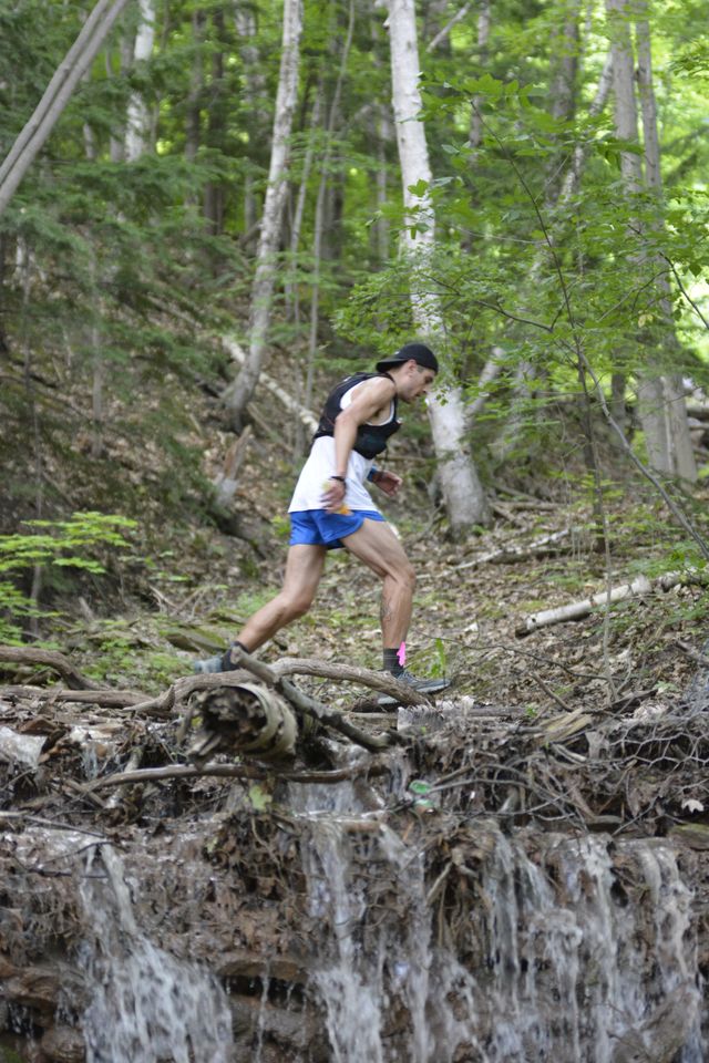 A man makes his way up the mountain, passing a watefall along his race to the top.