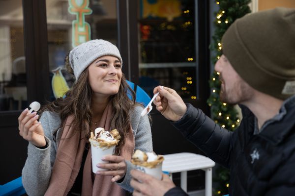 Couple sitting outside Royal Majesty Espresso Bar, eating the decadent topping on their S'mores Latte during Holiday Magic in the Village.