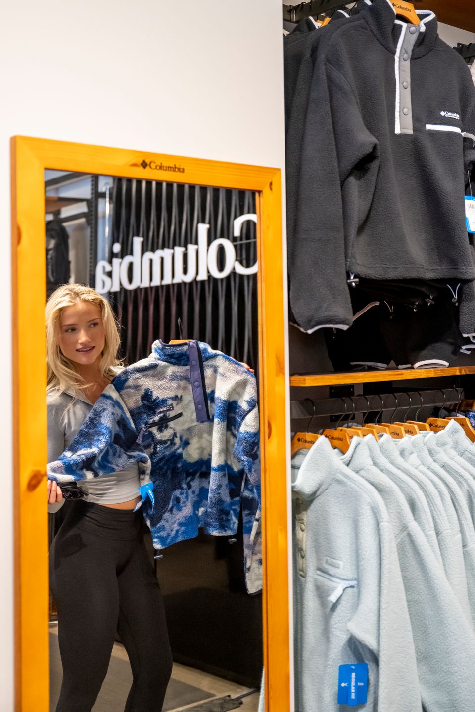 A young woman holding up a fleece sweater in the mirror on a shopping trip at Columbia Sportswear in Blue Mountain Village