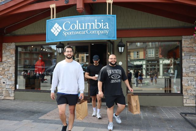 3 guys walking out of the Columbia Sportswear store front carrying shopping bags.