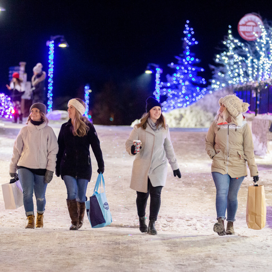 Group of friends shopping in the village at night, with the streets illuminated with holiday lights.