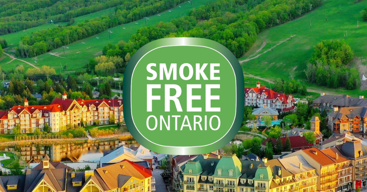 A beautiful aerial shot of the Village with vibrant yellows on the buildings and green mountains, with the Smoke Free Ontario logo overlaying the photo.