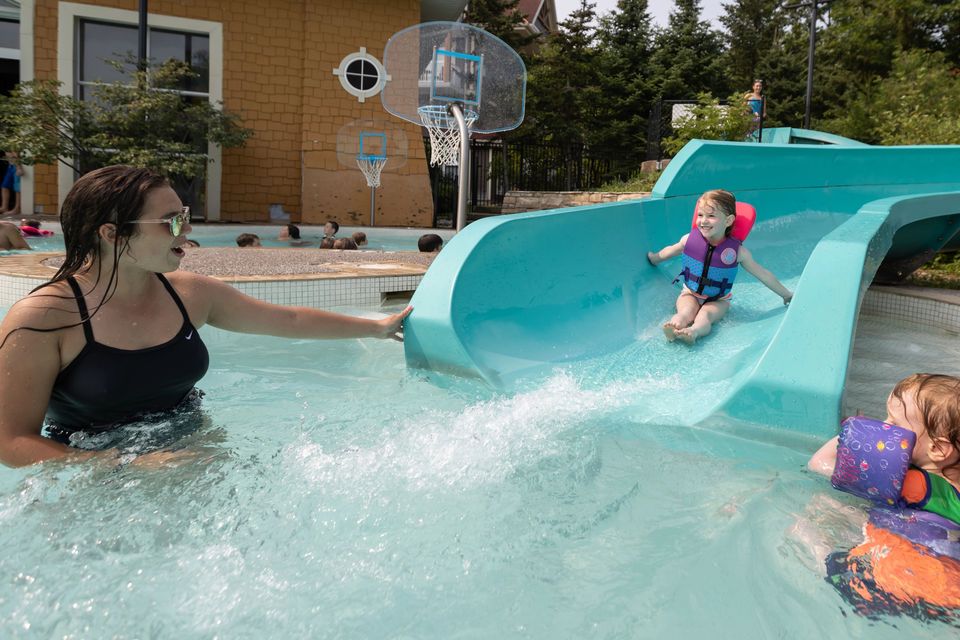 Young girl speeding down the outdoor waterslide at Plunge with her mom waiting to catch her. 