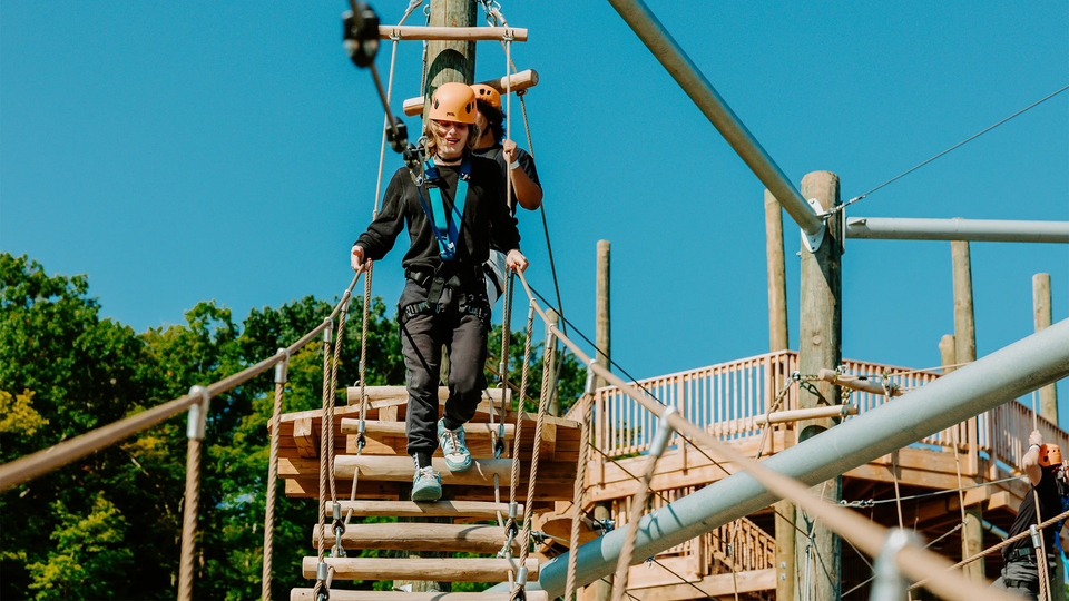 A man carefully conquers an exhilarating high ropes course suspended safely over the water below at the Blue Mountain Resort Skywalk Challenge High Ropes Course