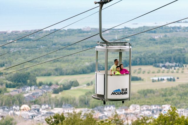 A family of 3 ascend up the mountain with stunning views of south georgian bay, on Ontario's only Open-Air Gondola at Blue Mountain Resort.