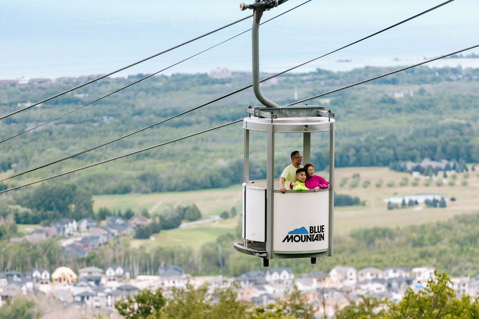 A family of 3 ascend up the mountain with stunning views of south georgian bay, on Ontario's only Open-Air Gondola at Blue Mountain Resort.