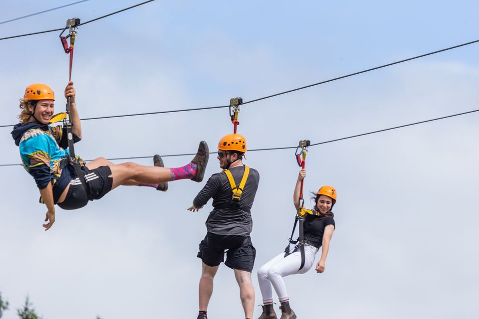 A group of three friends soaring smoothly through the air at exhilarating speeds of up to 50 km/h on the Wind Rider Trip Zips course at Blue Mountain Resort Explore Park