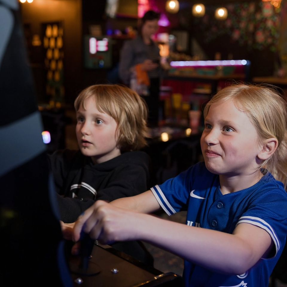 Two young kids battling it out on the retro arcade console at The Bunker Retro Gaming Lounge in Blue Mountain Village.