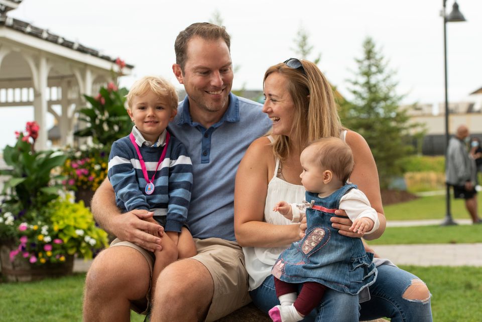 Mom, dad, and their two tiny kids smiling together on a beautiful sunny day in the Village.