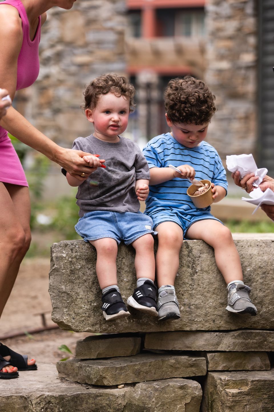 Two adorable toddlers eating ice cream on the bench with ice cream all over their faces.