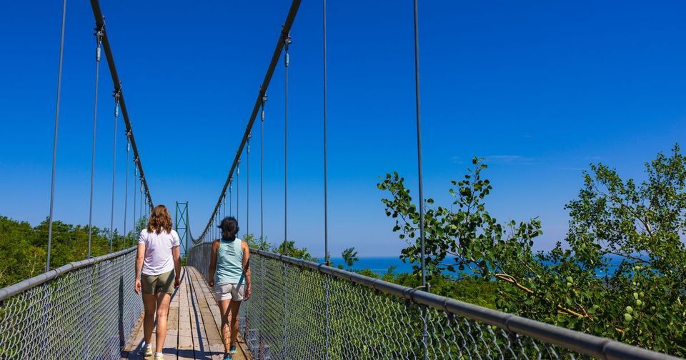 Two friends walk across the iconic suspension bridge at Scenic Caves Nature Adventures, adjacent to Blue Mountain Resort