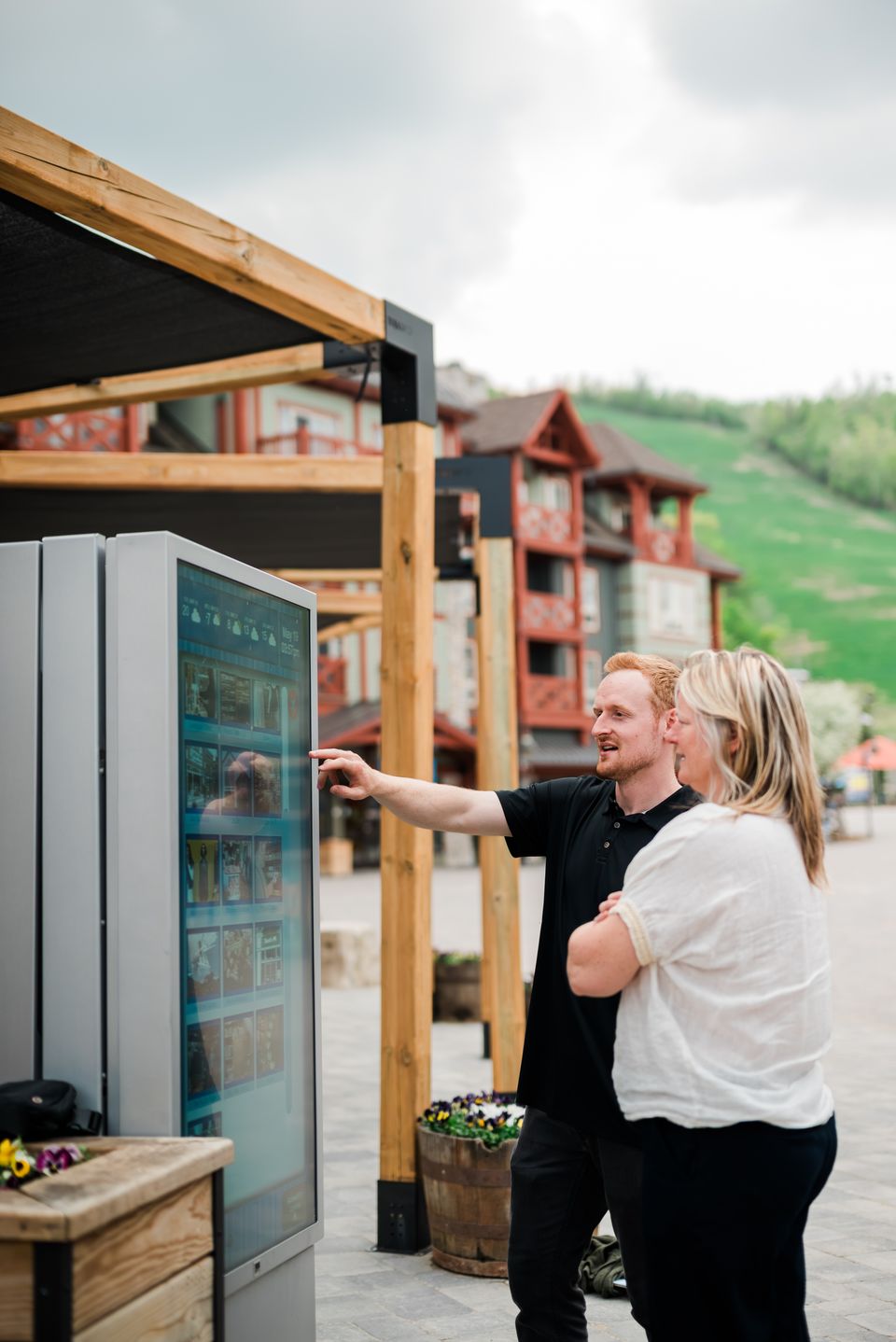 Two friends pointing and interacting with the digital kiosk sign for more information to navigate their next adventure at Blue Mountain Village.