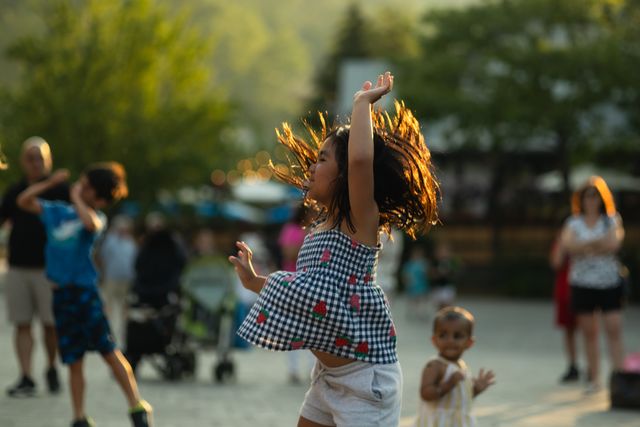 Young girl jumping and dancing with her hands in the air during Groove Dancing in the Village Events Plaza on a warm summer evening. 