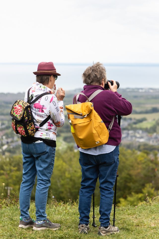 A couple mature friends taking photos of the view of the Village and Georgian Bay from the top of the Mountain.