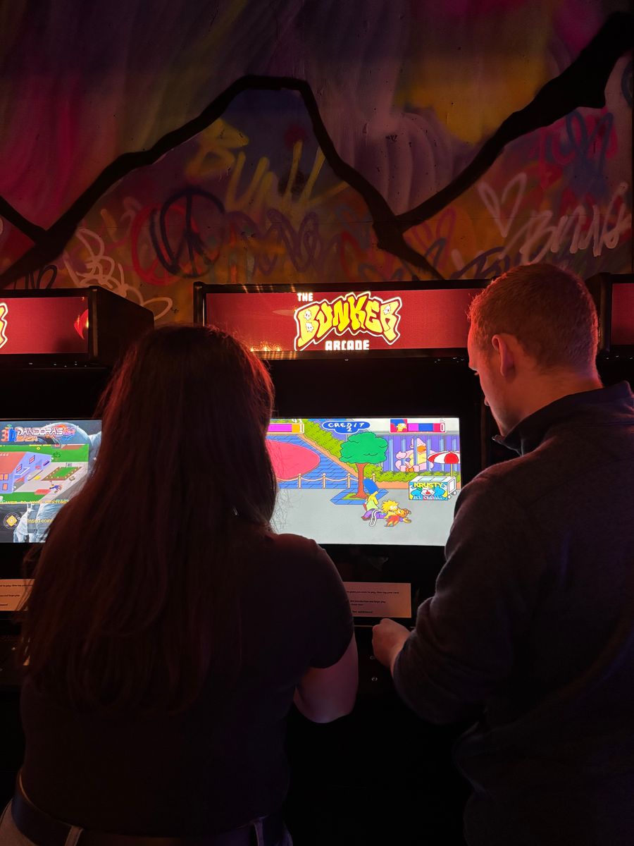 Couple battling it out playing The Simpsons on a retro arcade console at The Bunker Arcade. 